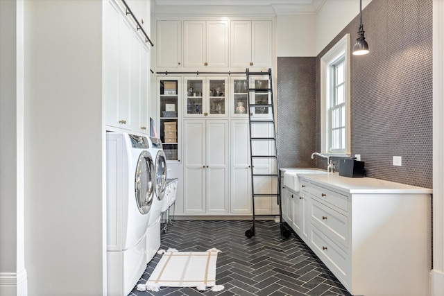 laundry area with a barn door, brick floor, a sink, cabinet space, and washer and clothes dryer