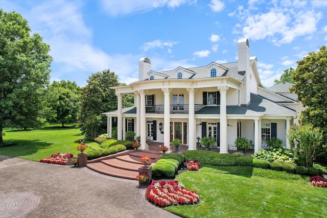 greek revival inspired property featuring a balcony, roof with shingles, a chimney, and a front yard