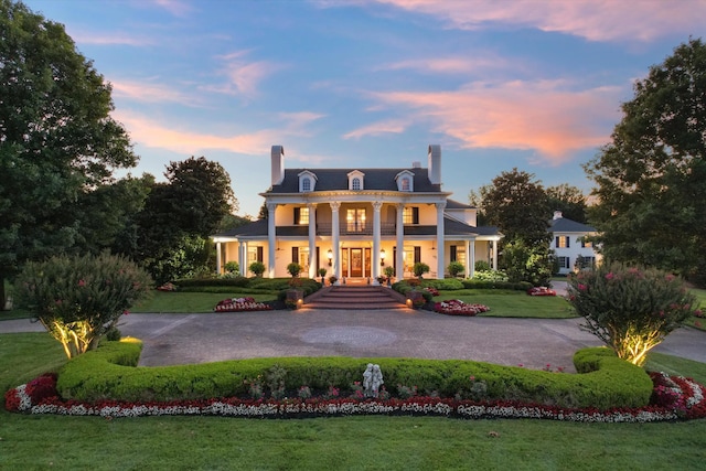 neoclassical home featuring covered porch, a yard, aphalt driveway, and a chimney