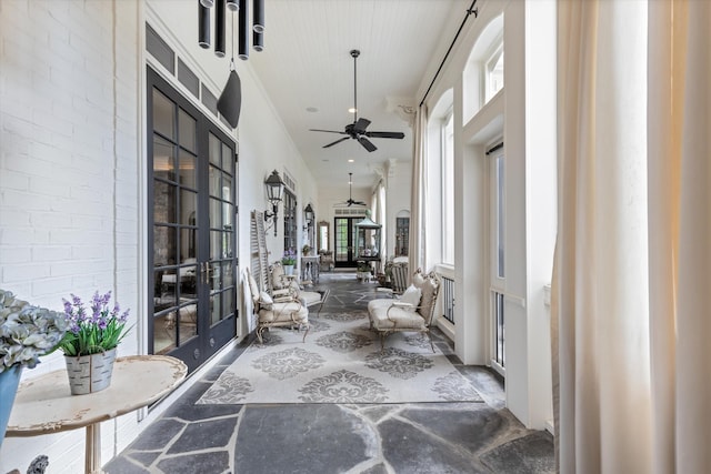 hall with brick wall, crown molding, a wealth of natural light, and french doors