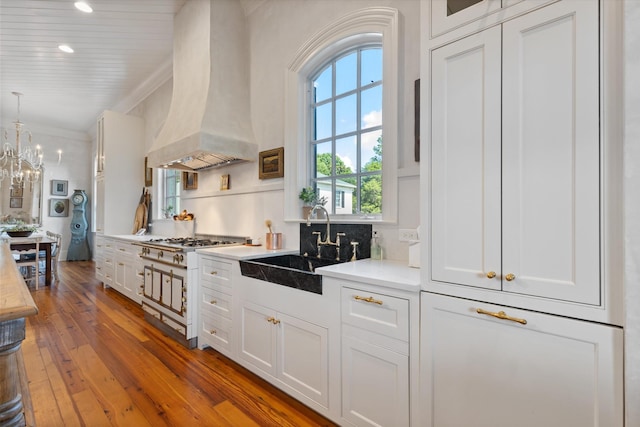 kitchen with pendant lighting, light countertops, premium range hood, and white cabinetry