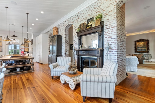 living room featuring a brick fireplace, light wood-style floors, crown molding, and recessed lighting