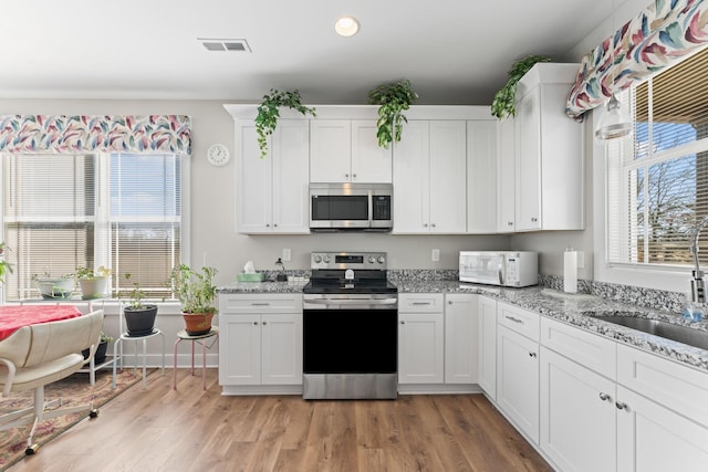 kitchen with appliances with stainless steel finishes, a sink, light stone countertops, and white cabinets