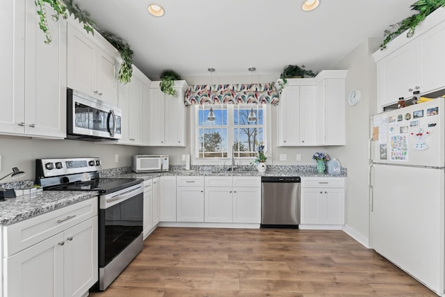 kitchen featuring stainless steel appliances, white cabinetry, a sink, and light stone counters