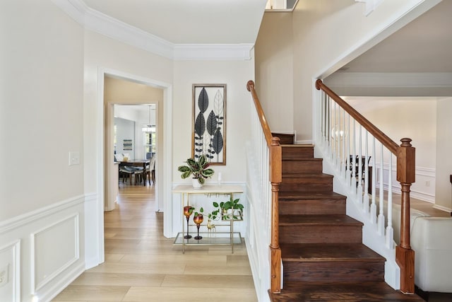 stairs with a wainscoted wall, ornamental molding, a decorative wall, and wood finished floors