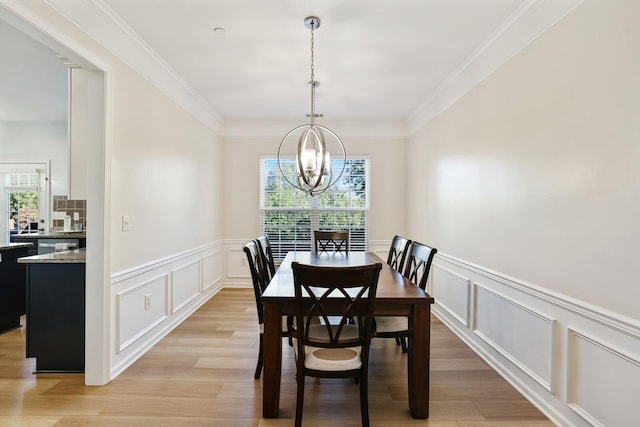 dining area featuring an inviting chandelier, ornamental molding, light wood finished floors, and a decorative wall