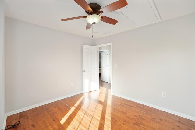 empty room with attic access, baseboards, ceiling fan, and wood finished floors