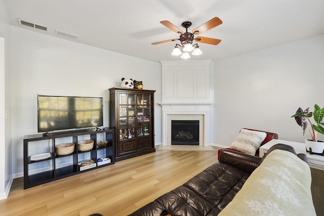 living area featuring visible vents, a large fireplace, ceiling fan, wood finished floors, and baseboards