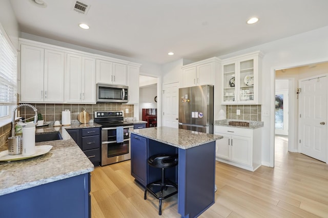 kitchen featuring a kitchen island, visible vents, white cabinetry, appliances with stainless steel finishes, and glass insert cabinets