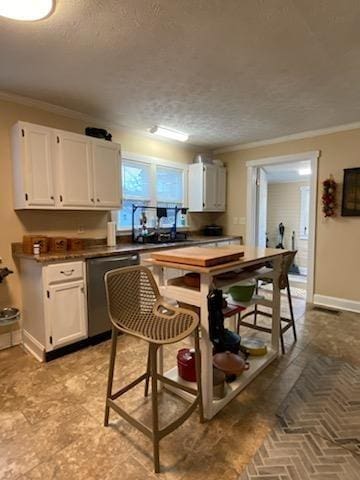 kitchen featuring baseboards, dark countertops, ornamental molding, white cabinetry, and stainless steel dishwasher