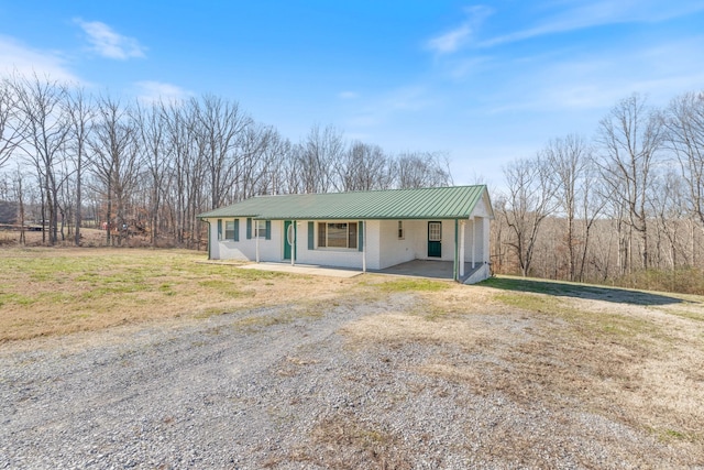 view of front facade featuring dirt driveway, metal roof, an attached carport, covered porch, and brick siding