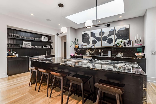 bar with a sink, stainless steel gas stovetop, wet bar, light wood finished floors, and pendant lighting