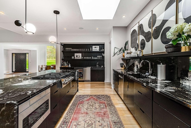 kitchen with open shelves, light wood finished floors, appliances with stainless steel finishes, pendant lighting, and a sink