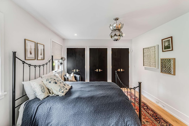 bedroom with multiple closets, baseboards, a chandelier, and wood finished floors