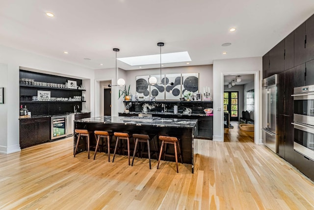 kitchen with beverage cooler, appliances with stainless steel finishes, decorative light fixtures, a kitchen bar, and open shelves