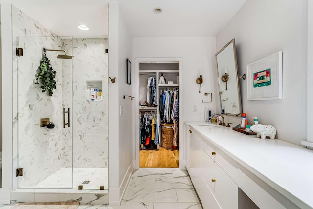 full bathroom featuring marble finish floor, a spacious closet, a marble finish shower, and vanity