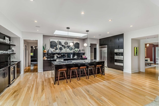 kitchen with dark cabinets, stainless steel appliances, a breakfast bar, light wood-type flooring, and decorative light fixtures