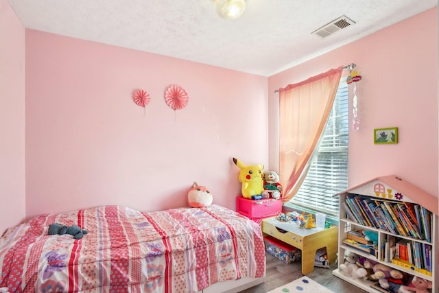 bedroom with a textured ceiling, visible vents, and wood finished floors