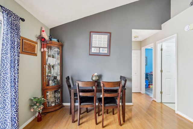 dining room featuring light wood-style flooring, baseboards, and vaulted ceiling