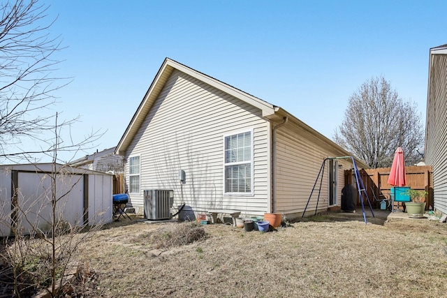 view of property exterior featuring central AC unit, fence, a storage unit, and an outbuilding