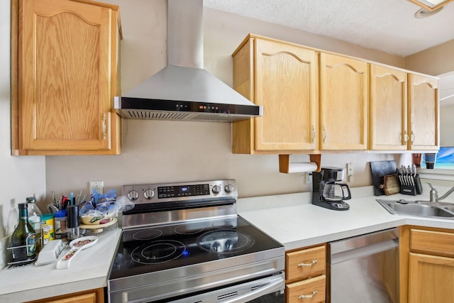 kitchen with light brown cabinets, stainless steel appliances, a sink, light countertops, and wall chimney range hood