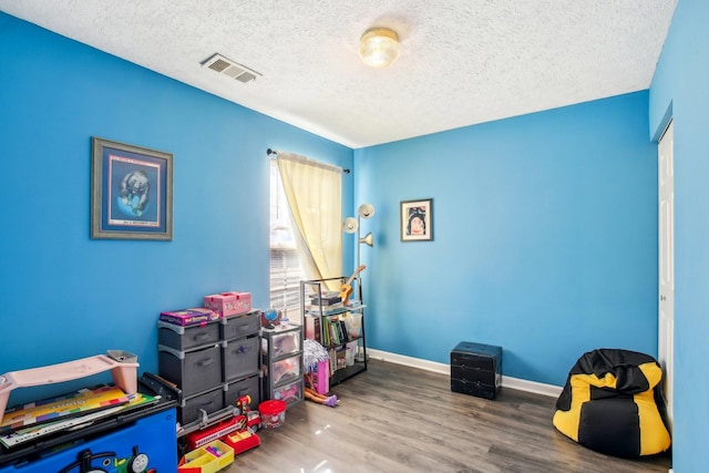 game room featuring a textured ceiling, wood finished floors, visible vents, and baseboards