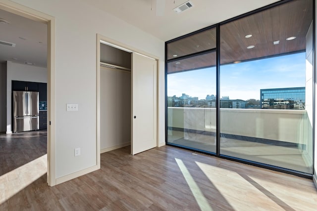 unfurnished bedroom with access to exterior, a city view, visible vents, light wood-style floors, and freestanding refrigerator