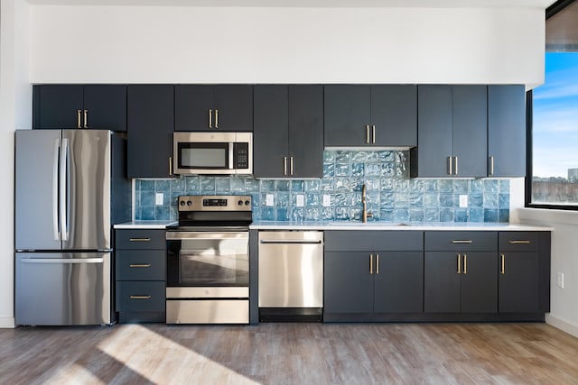 kitchen with tasteful backsplash, light wood-style flooring, appliances with stainless steel finishes, light countertops, and a sink