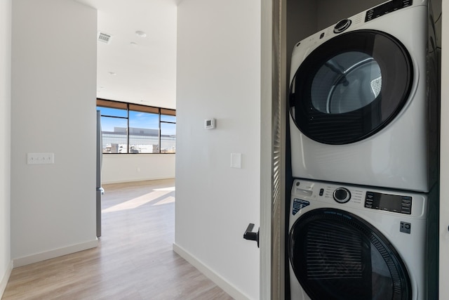 laundry area with light wood finished floors, visible vents, stacked washer / dryer, laundry area, and baseboards