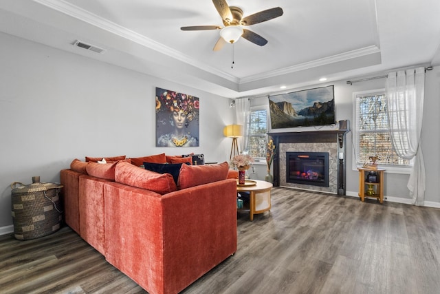 living room with visible vents, a raised ceiling, ornamental molding, wood finished floors, and a fireplace