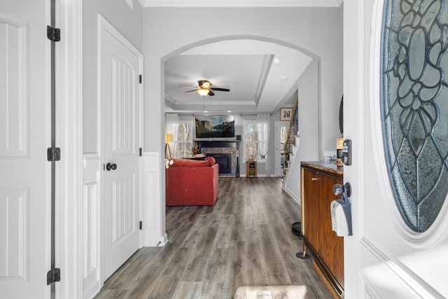 foyer entrance featuring arched walkways, a fireplace, wood finished floors, a ceiling fan, and crown molding