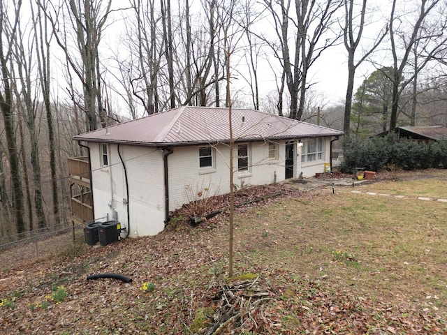 back of house featuring metal roof, brick siding, fence, and central air condition unit