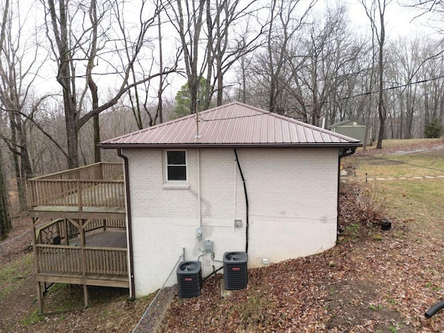 view of home's exterior featuring brick siding, metal roof, a wooden deck, and central AC unit