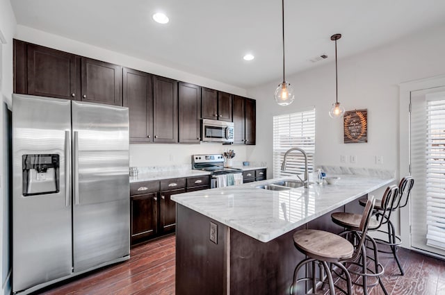 kitchen with dark brown cabinetry, stainless steel appliances, a breakfast bar, a sink, and visible vents