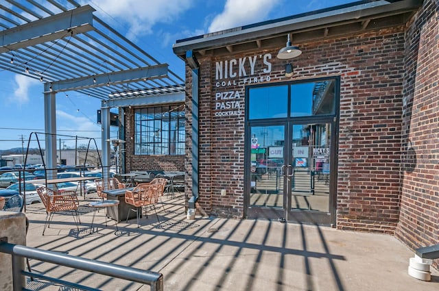 entrance to property featuring a patio, a pergola, and brick siding