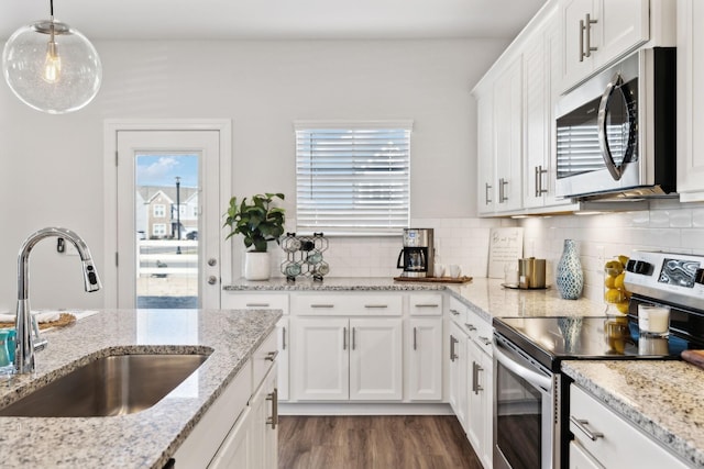 kitchen featuring decorative light fixtures, light stone countertops, stainless steel appliances, white cabinetry, and a sink