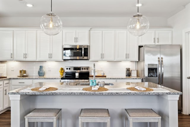 kitchen with appliances with stainless steel finishes, decorative light fixtures, a center island with sink, and white cabinetry