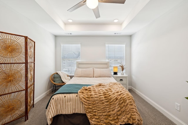 carpeted bedroom featuring a tray ceiling, visible vents, and baseboards