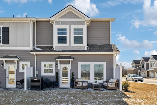 view of front facade featuring central AC unit, an outdoor hangout area, a patio, and roof with shingles