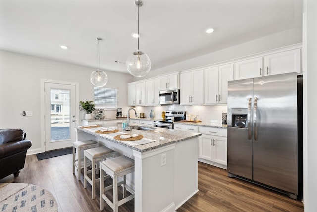 kitchen featuring stainless steel appliances, a sink, white cabinets, a center island with sink, and pendant lighting