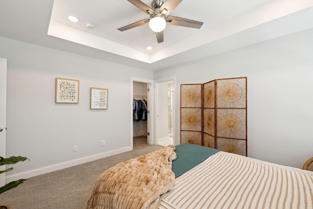 bedroom featuring light carpet, baseboards, a raised ceiling, a walk in closet, and recessed lighting