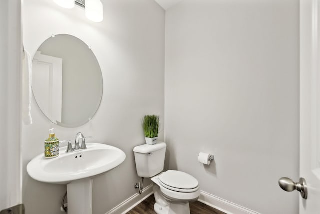 half bath with baseboards, toilet, and wood finished floors