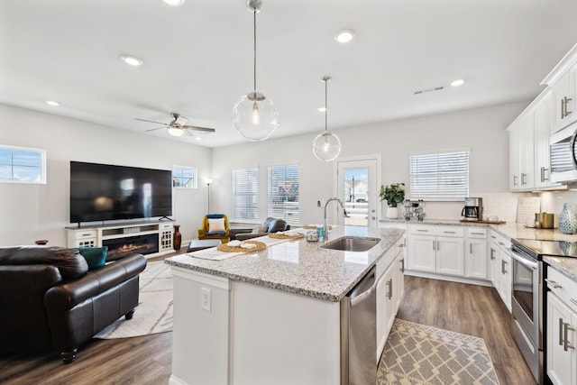 kitchen featuring decorative light fixtures, stainless steel appliances, white cabinets, a sink, and an island with sink