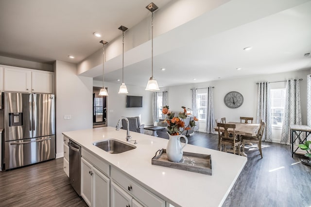 kitchen with stainless steel appliances, a sink, white cabinets, light countertops, and an island with sink