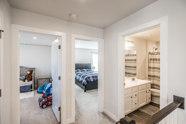 hallway with baseboards, a sink, and light colored carpet