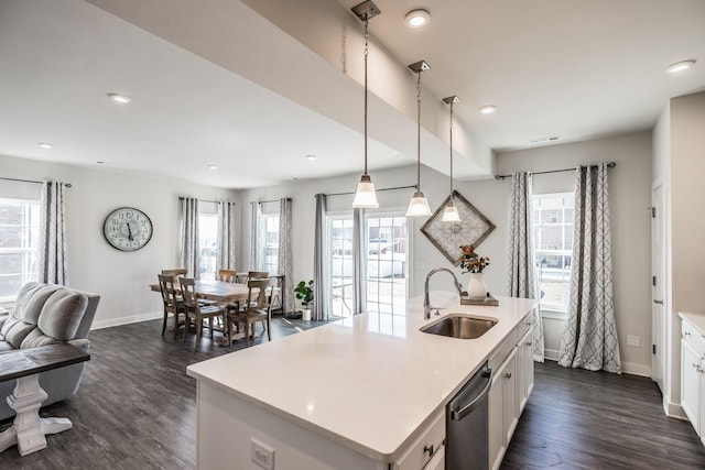 kitchen with decorative light fixtures, a center island with sink, light countertops, white cabinets, and a sink