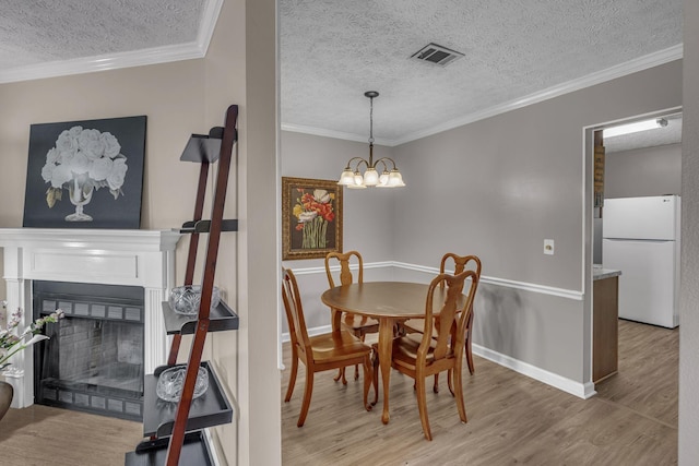 dining area with light wood finished floors, visible vents, ornamental molding, a textured ceiling, and a fireplace