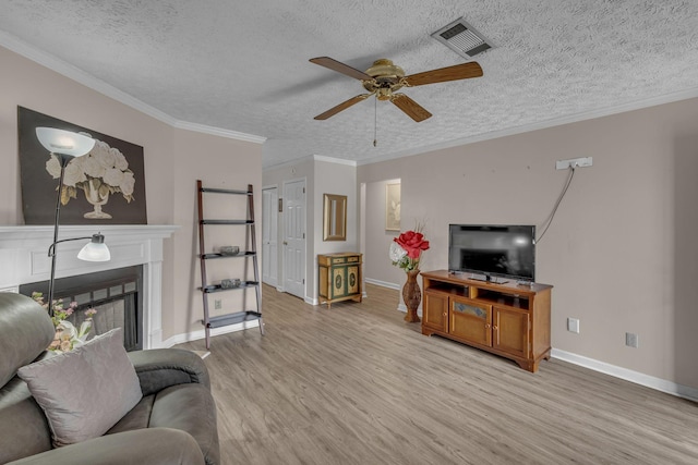 living area featuring a fireplace, crown molding, visible vents, light wood-style floors, and a textured ceiling