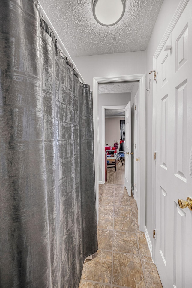 corridor featuring a textured ceiling, stone finish flooring, and baseboards