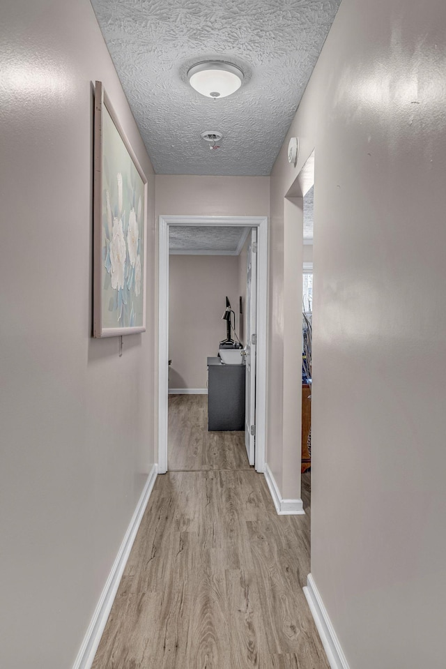 hall with a textured ceiling, baseboards, and wood finished floors